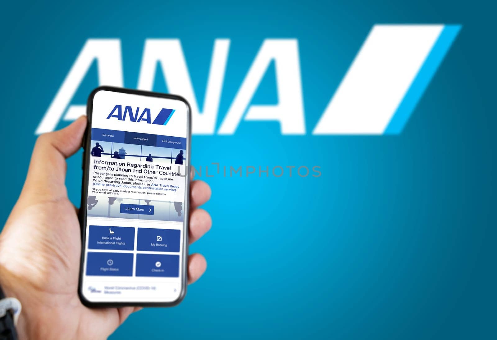 Tokyo, JAP, January 2022: Hand holding a phone with ANA All Nippon Airways flight booking application. Ana logo blurred on a blue background. Booking airline tickets