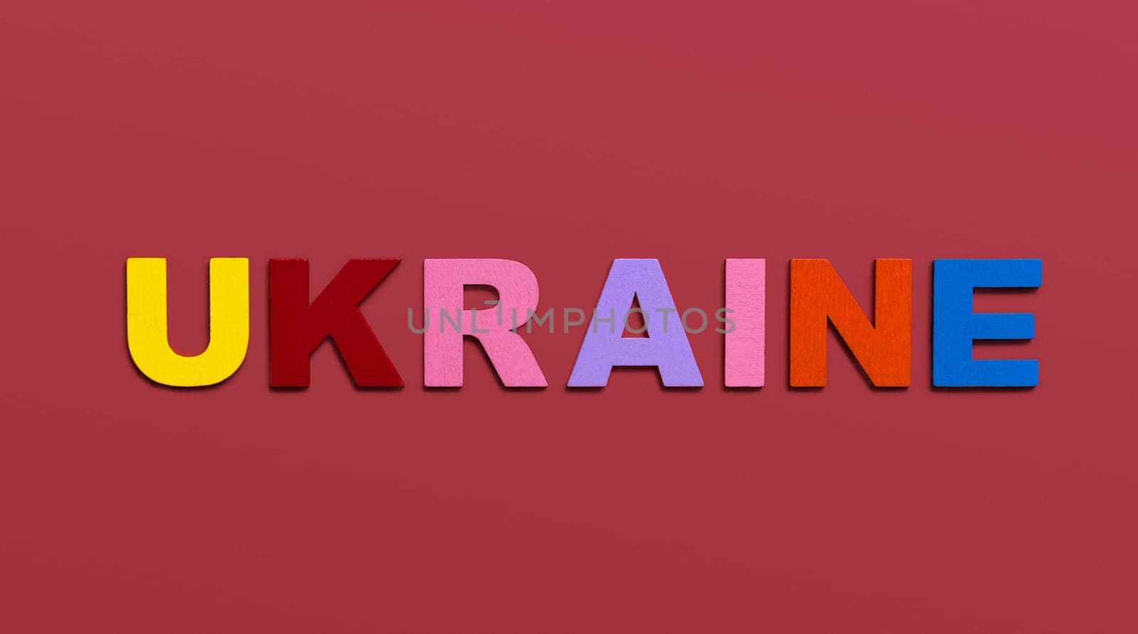 Ukraine, word written in colorful wooden alphabet letters on red background. The concept of a terrible war for independence. Top view. Copy space