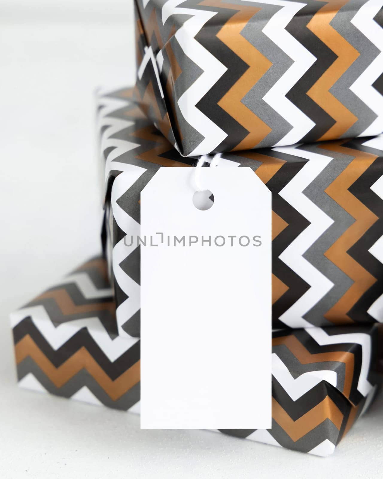 Presents with blank vertical gift tag close up. Gift boxes wrapped in chevron geometric paper. Christmas, New Year, Birthday, Anniversary label mockup