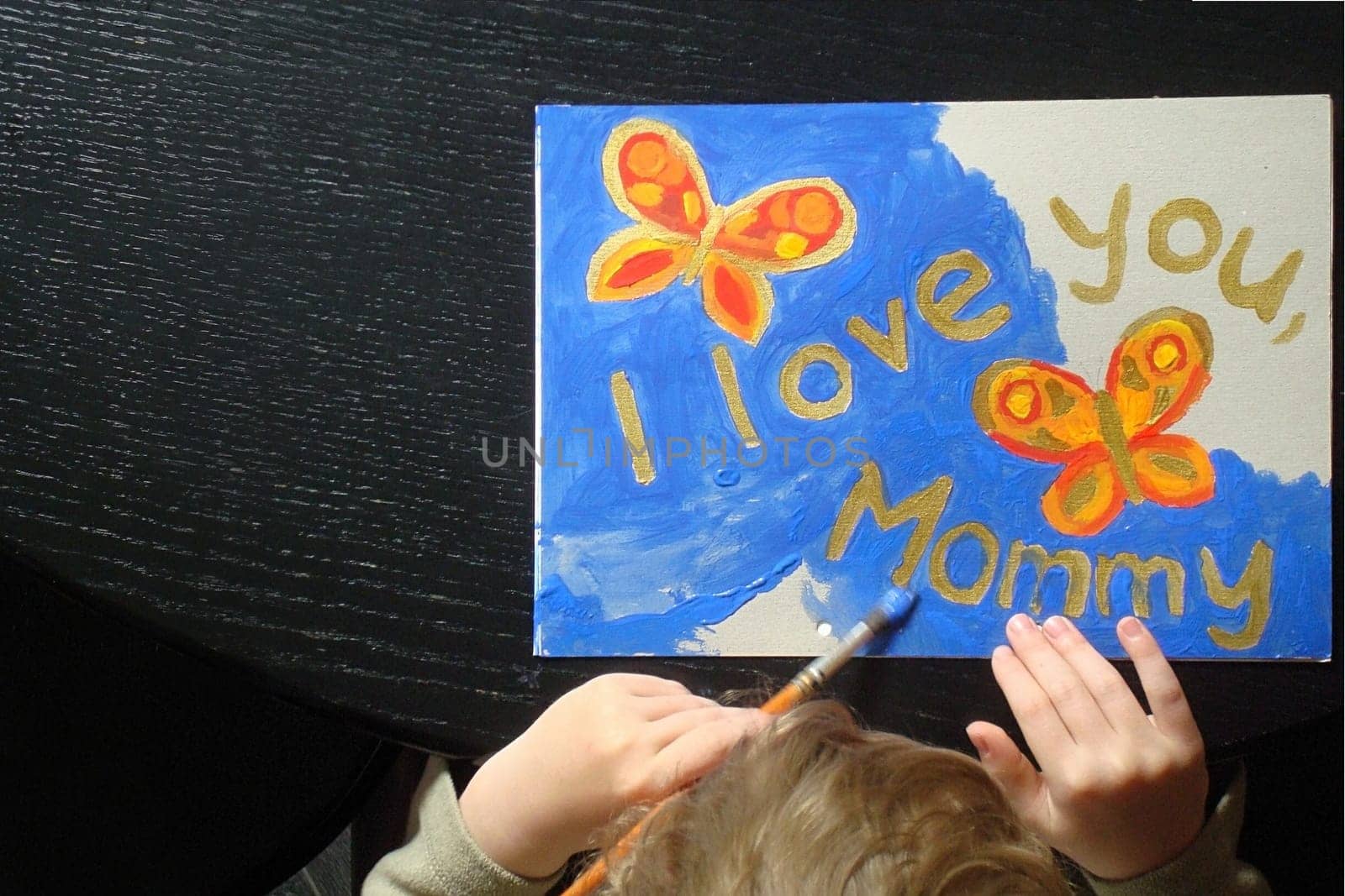hand of a little child painting a picture with butterflies for mommy at mother's day with the text I love you mommy