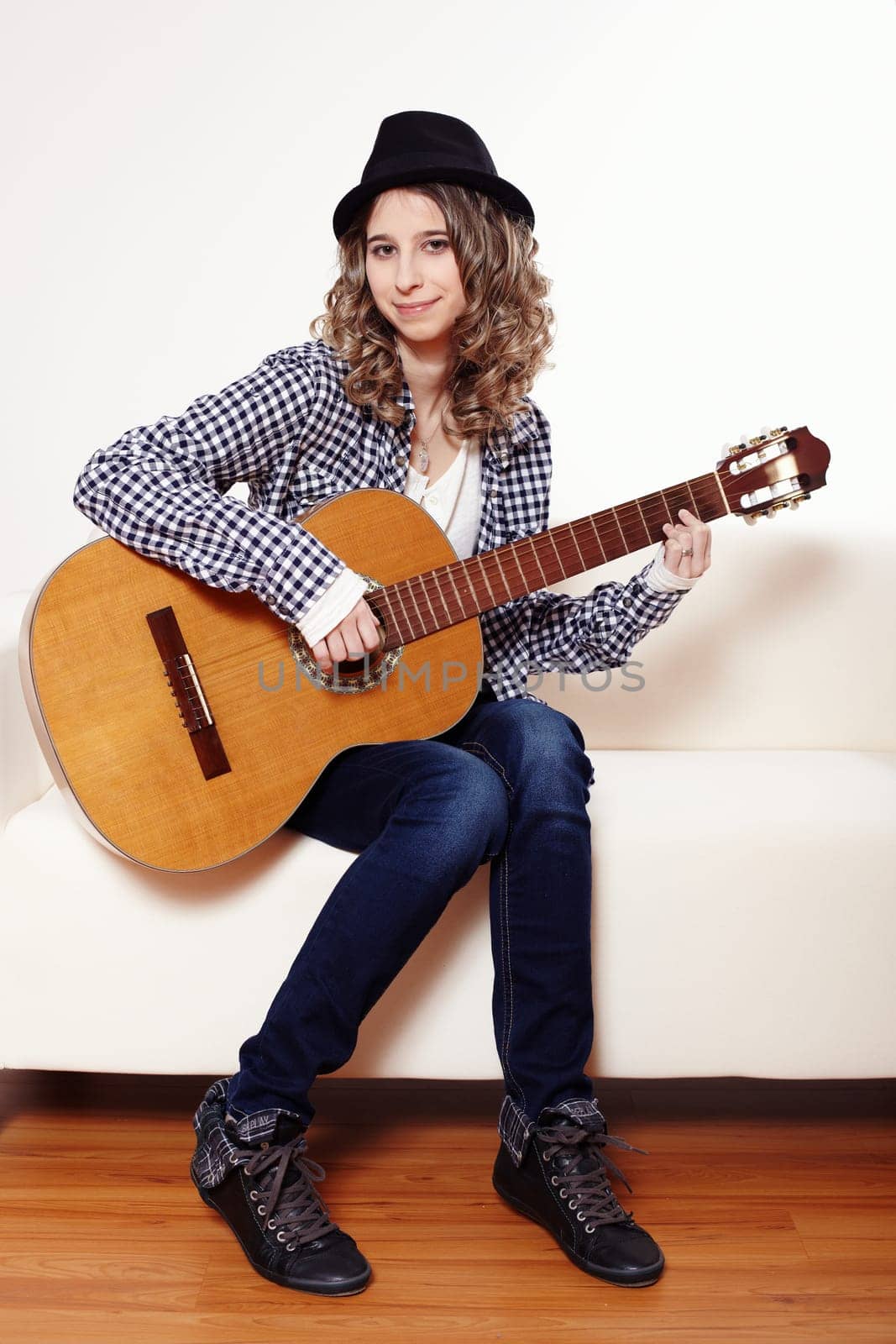 Young woman playing the guitar and sitting on a sofa