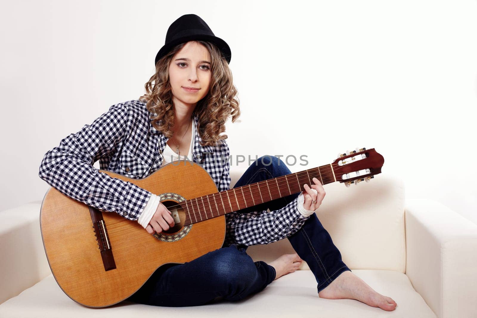 Young woman playing the guitar and sitting on a sofa