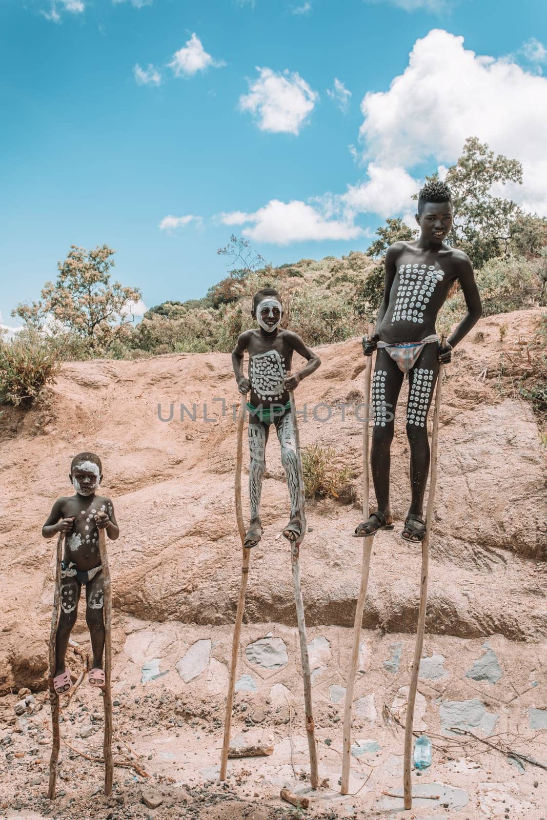 Southern Nations region, Ethiopia - May 10, 2019: Unknown happy Banna boy with traditional body painting walking on stilts in Southern Nations region, Ethiopia