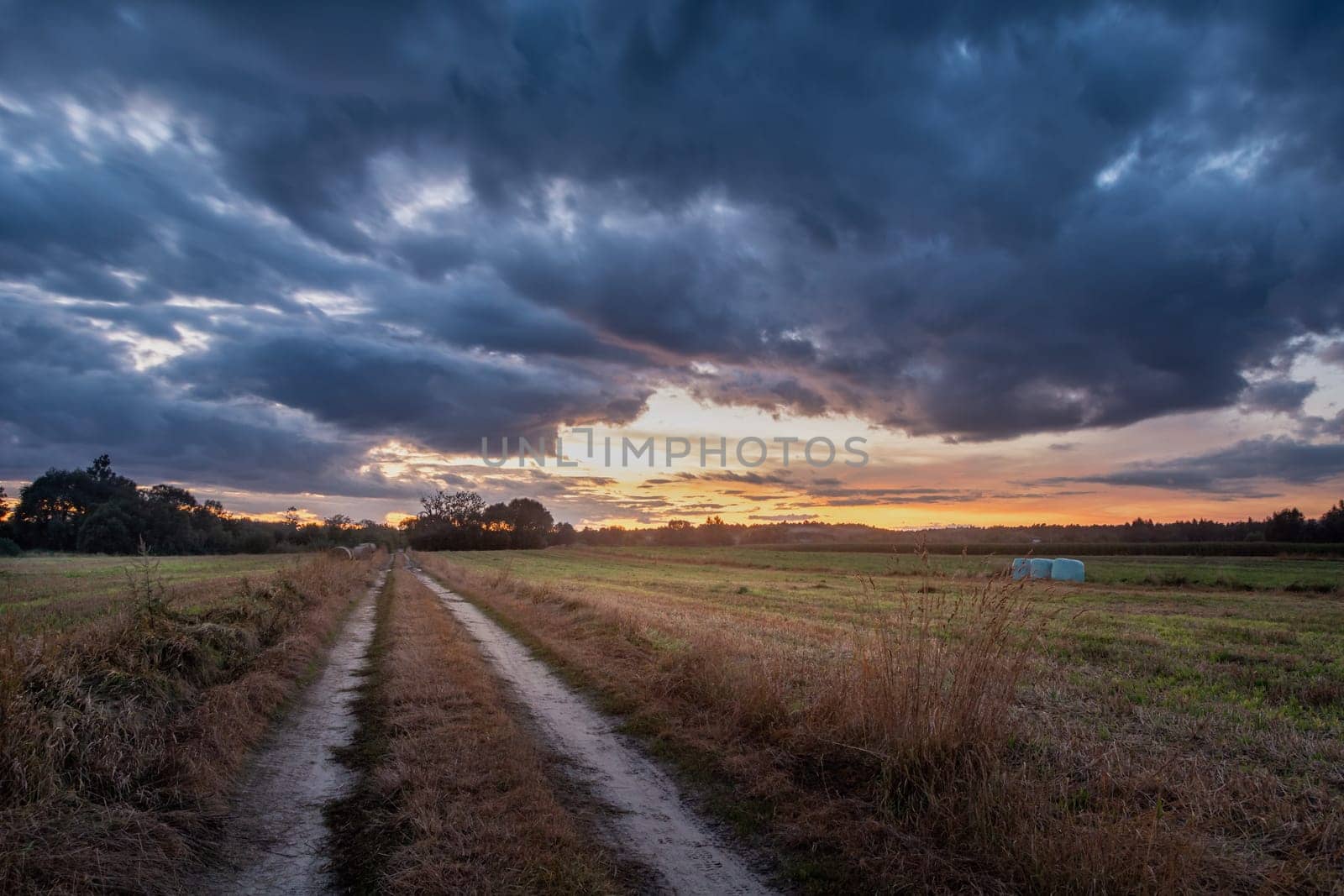 Dirt road through the field and clouds after sunset, summer view