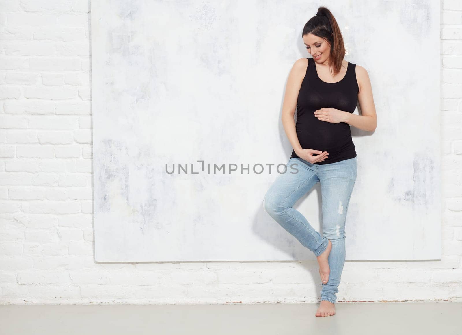 Fashion portrait of happy pregnant woman in jeans.. against white wall with copyspace.