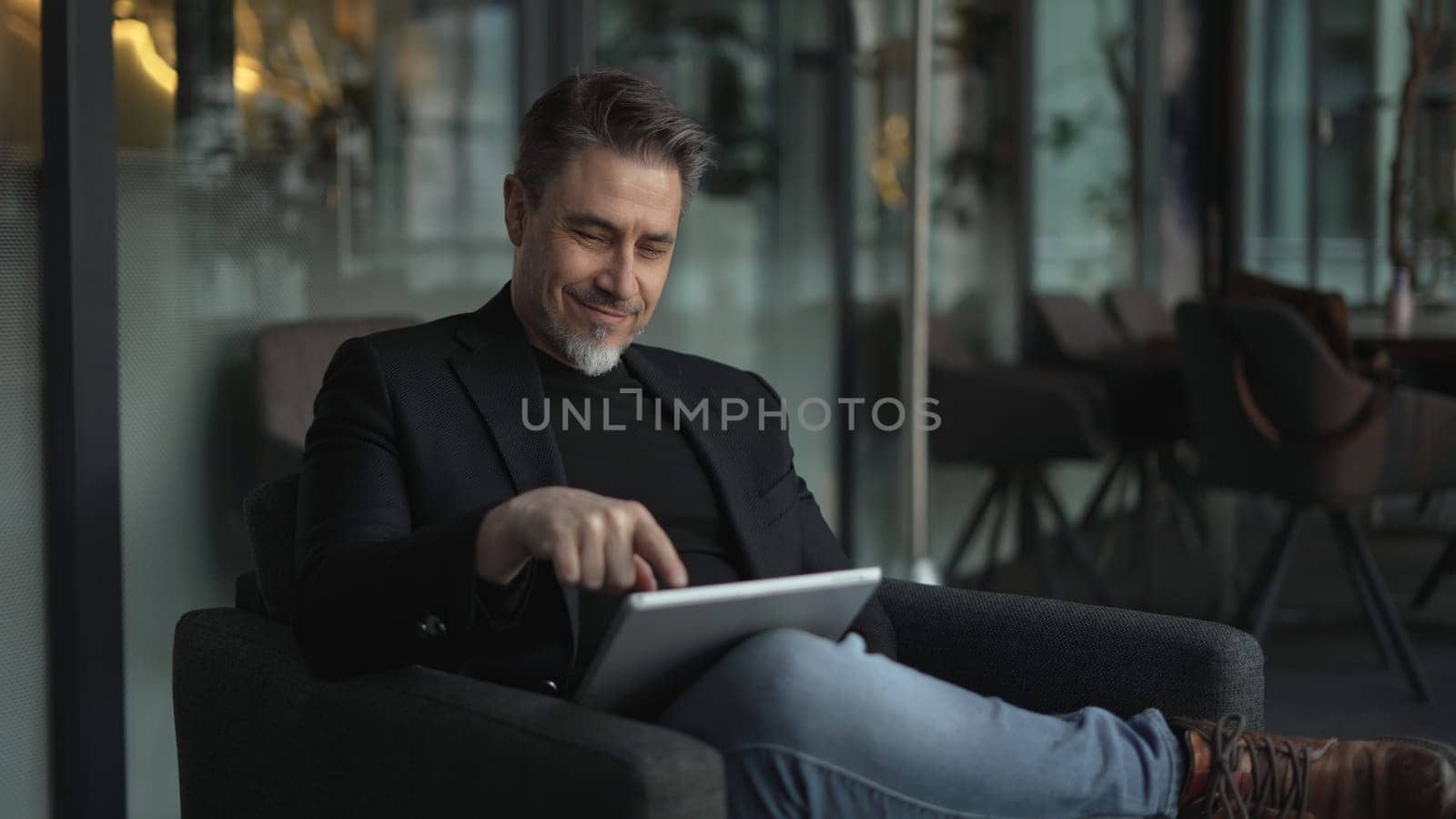 Businessman using tablet computer in office. Happy middle aged man in business casual, Entrepreneur working online, reading finance report, thinking.