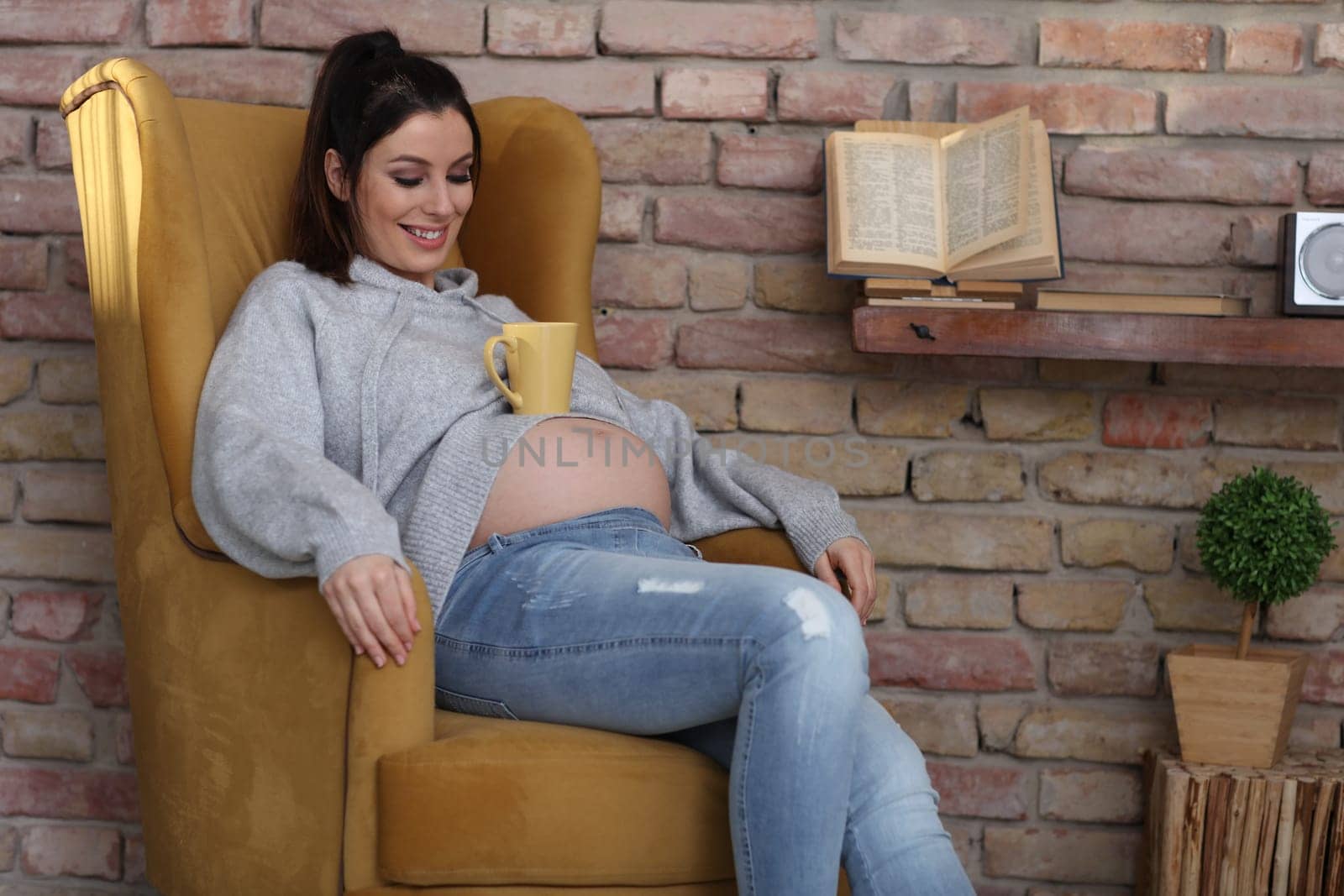 Happy pregnant woman at home relaxing in armchair holding cup of tea.