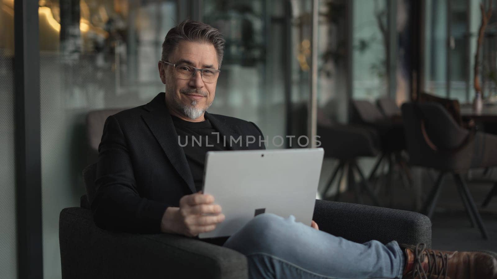Business portrait - businessman using tablet computer in office lobby or on cafe terrace. Happy middle aged man, entrepreneur working online.