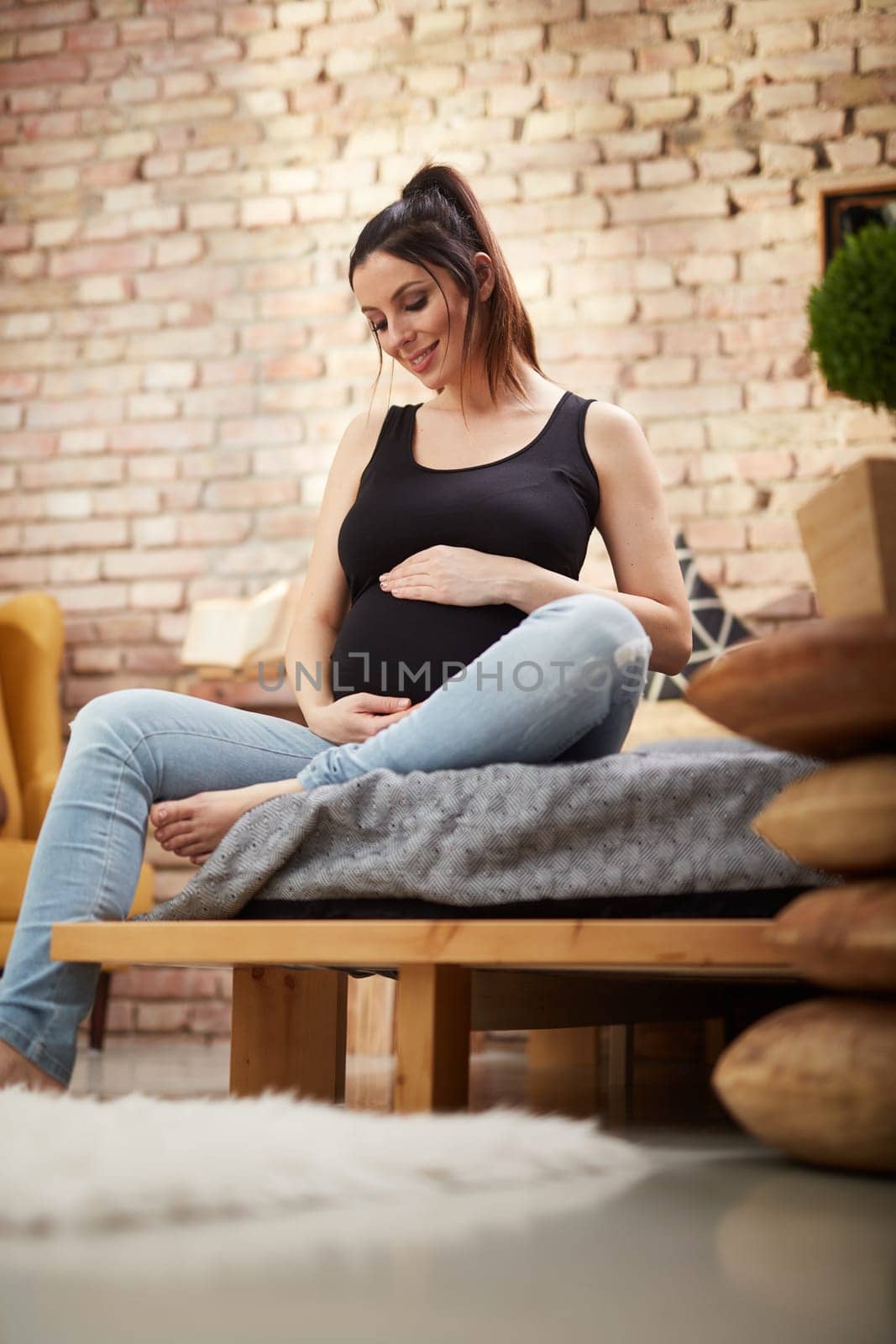 Happy pregnant woman sitting on bed at home smiling, relaxing.