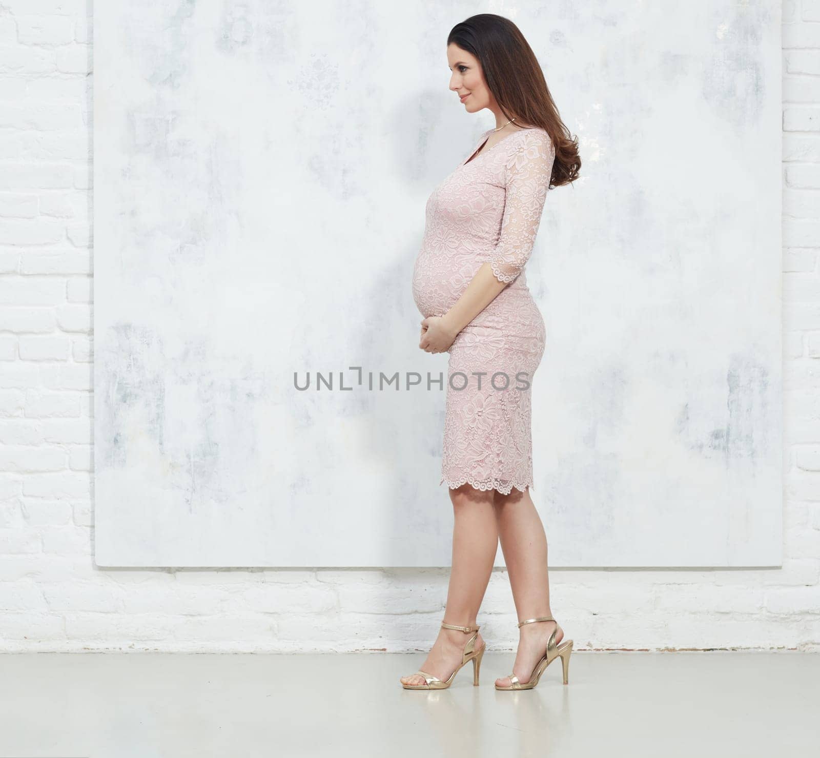 Fashion portrait of happy pregnant woman in elegant dress against white wall with copyspace.