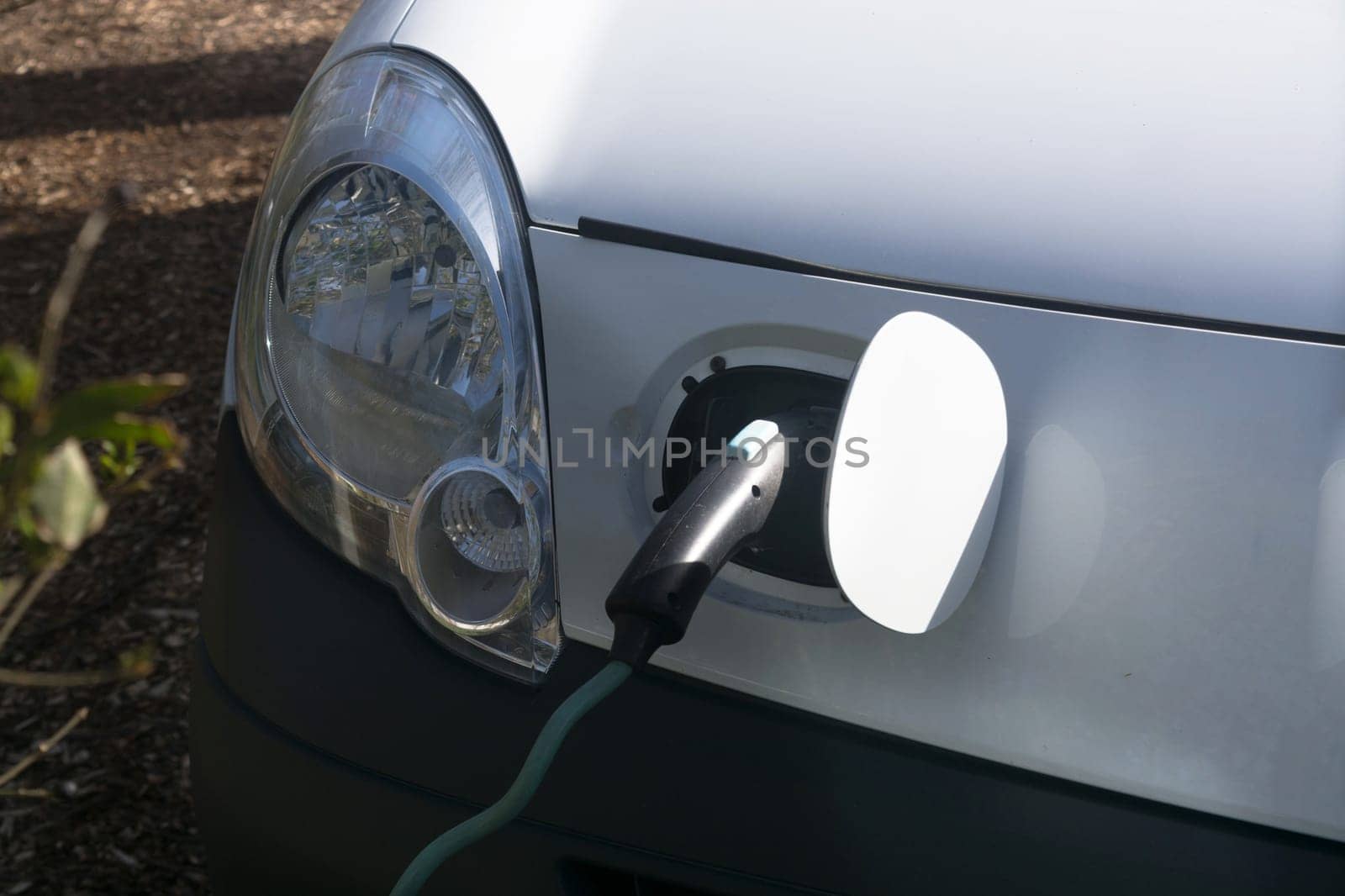 EV car or electric vehicle at the charging station with the power cord adapter plugged into blurred nature with blue energy power effect. Environmentally friendly sustainable energy concept. .