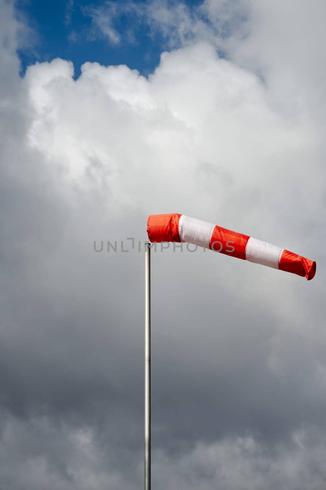 red windsock/ textile tube on a stormy sky at daytime, daylight, dark clouds with the sun breaking through