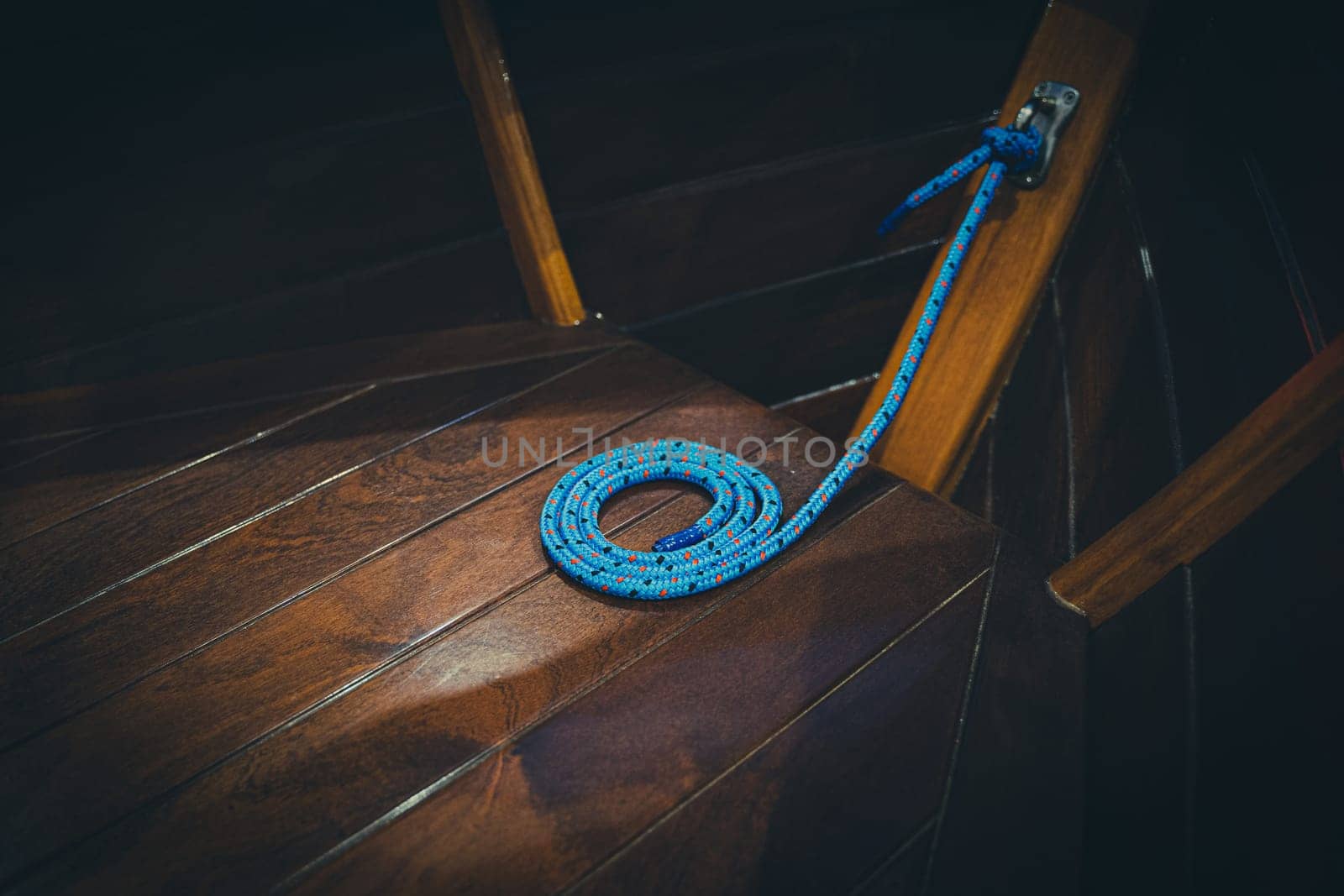 closeup of blue rope arranged in a spiral shape on the wooden brown deck of a sailing yacht