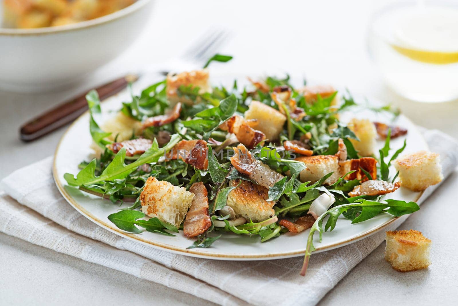 Dandelion salad with roasted bacon and croutons on grey background close up