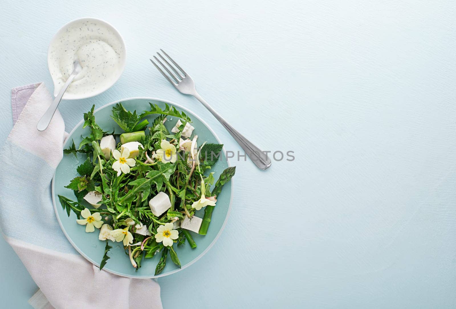 Spring salad with dandelion, asparagus, flowers, nettle and cream cheese. Healthy spring detox food ingredients.