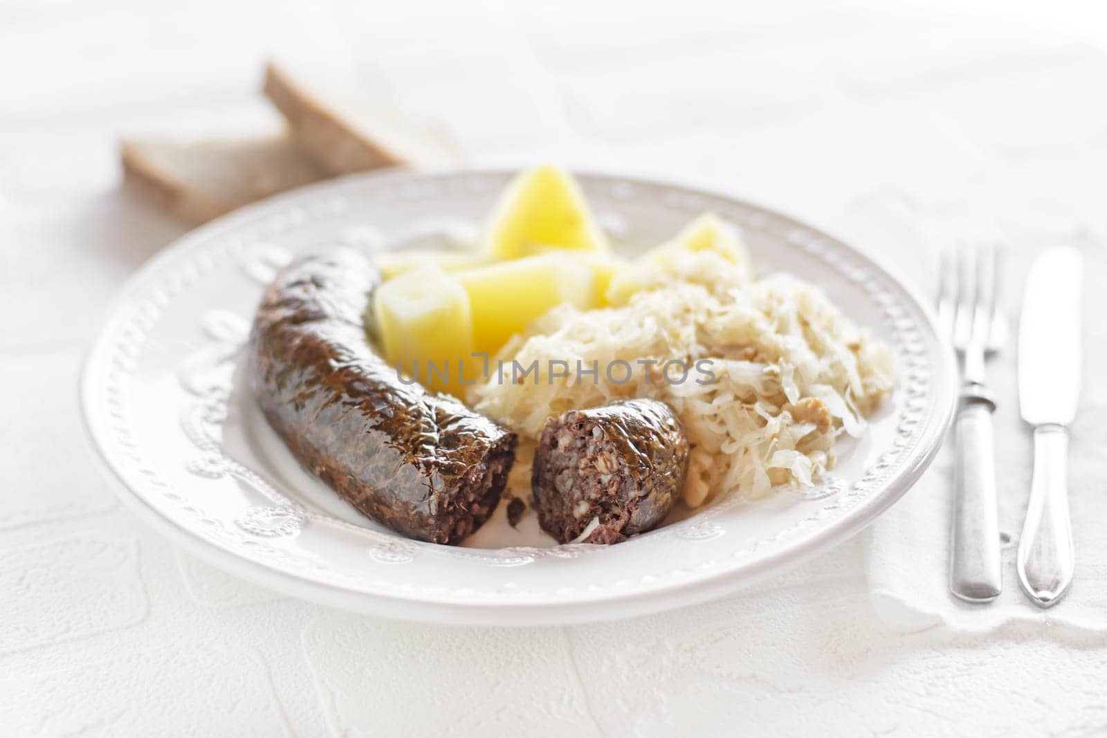 Bloody sausage and stewed sauerkraut with cooked potatoes close up. Traditional Slovenian dish with roasted bloody sausage