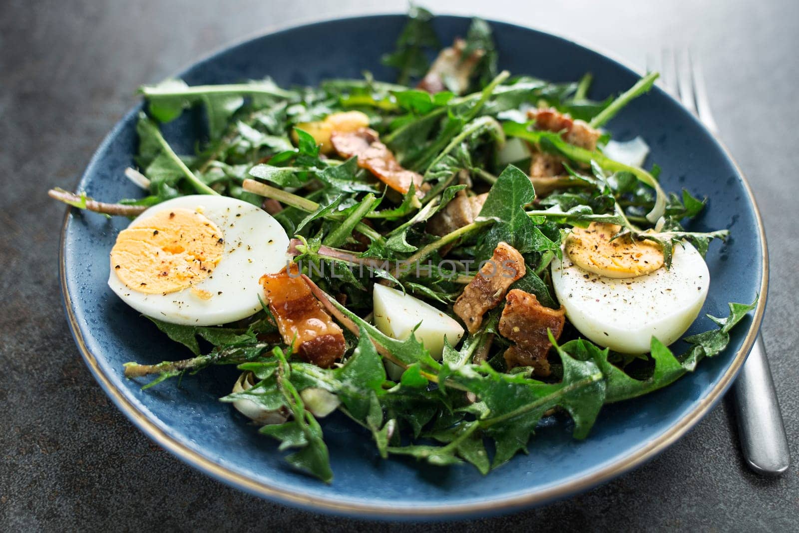 Dandelion salad with eggs and roasted bacon close up