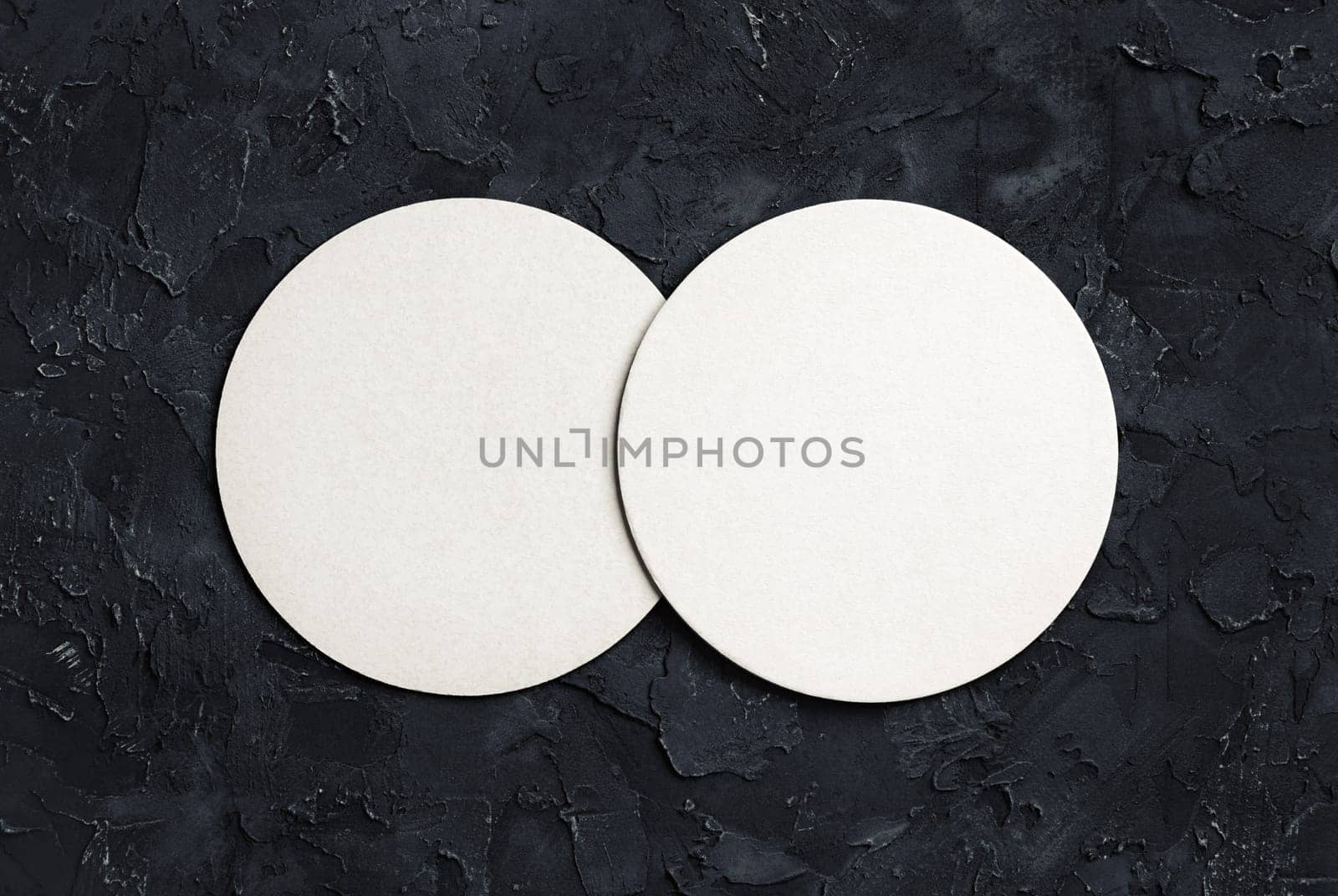 Blank white beer coasters on black plaster background. Top view.