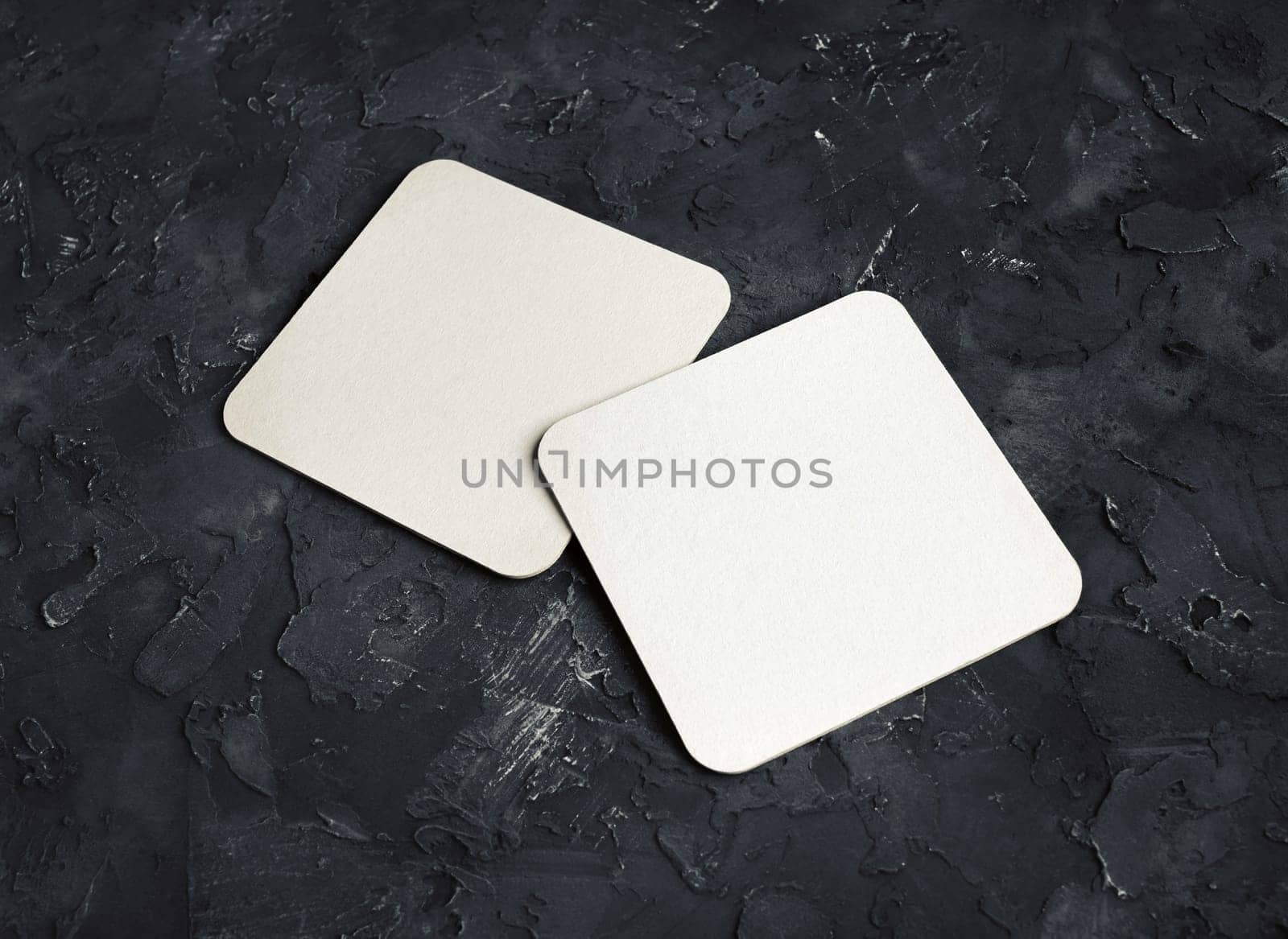 Blank white square beer coasters on black plaster background.