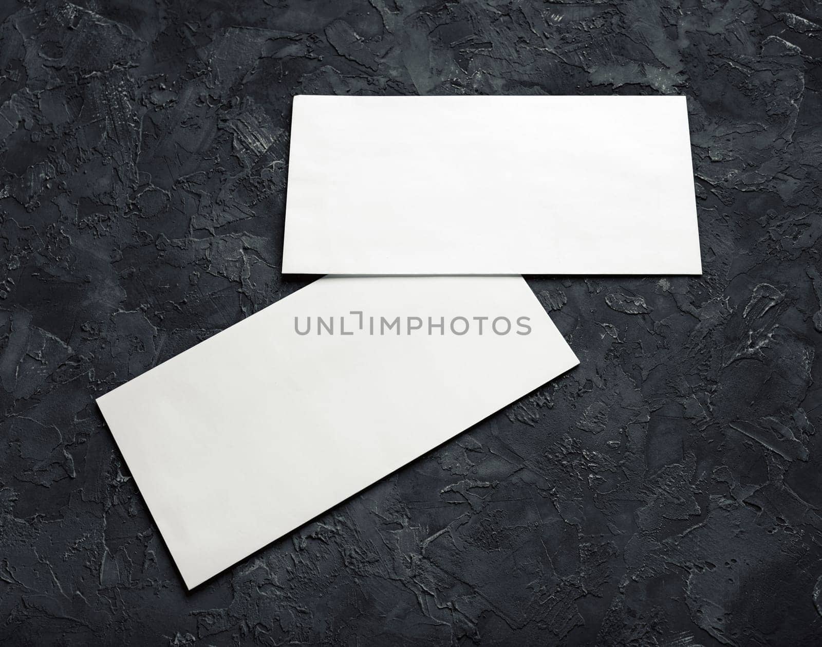 Two blank paper envelopes on black plaster background. Template for branding identity.