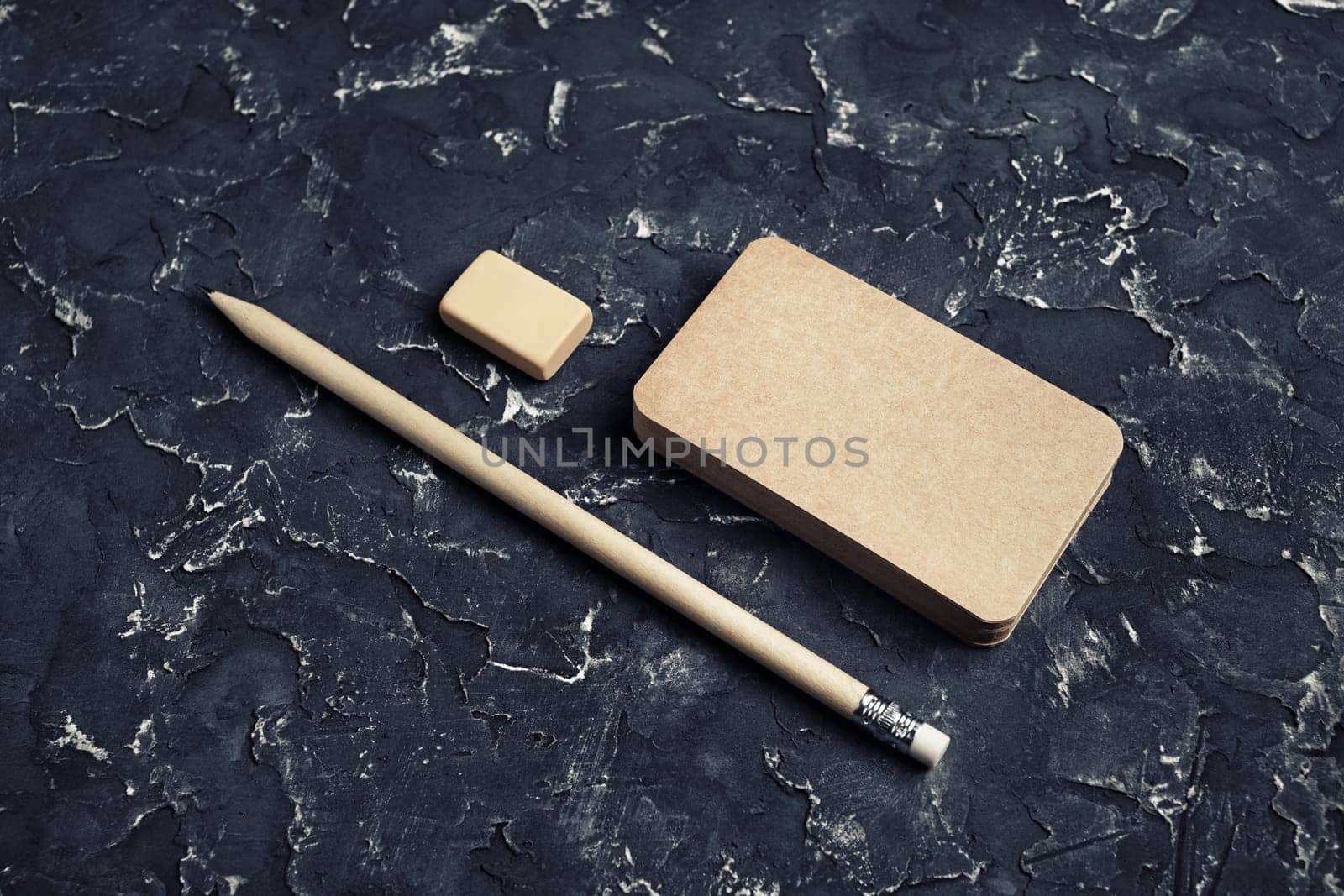 Photo of blank kraft business card, pencil and eraser on black plaster background.