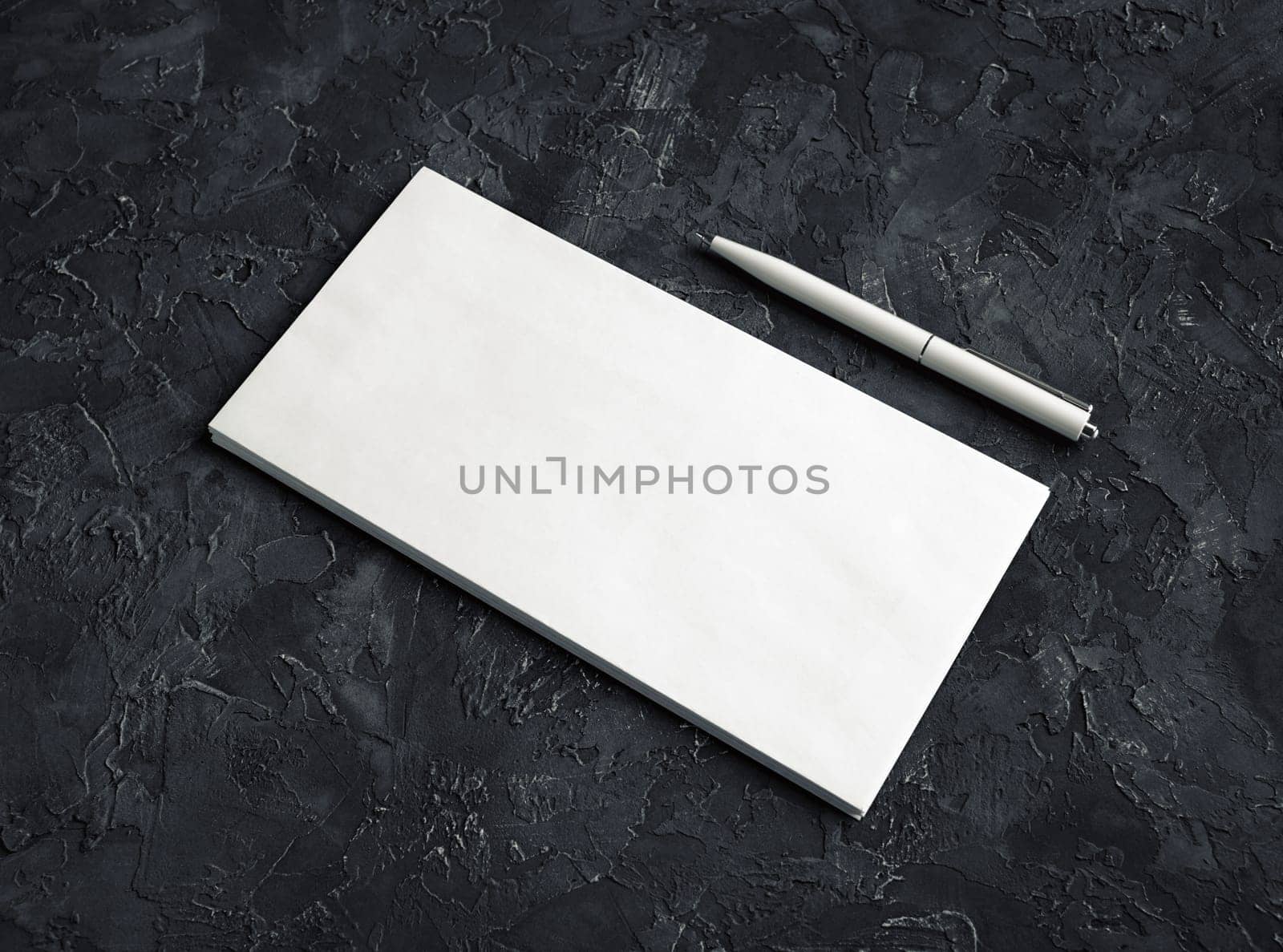 Photo of blank paper envelope and pen on black plaster background. Template for your design.