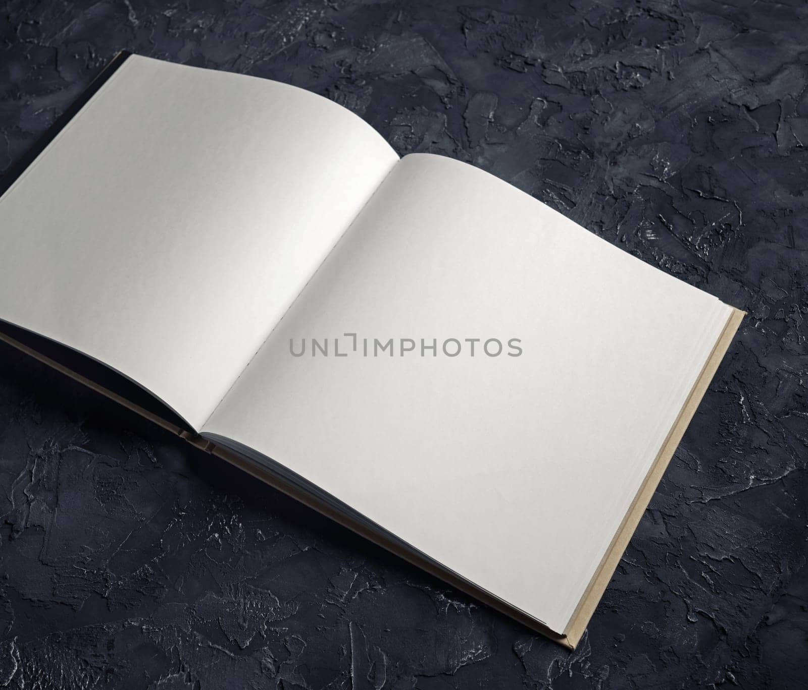 Photo of blank opened notebook on black plaster background. Template for graphic designers portfolios.