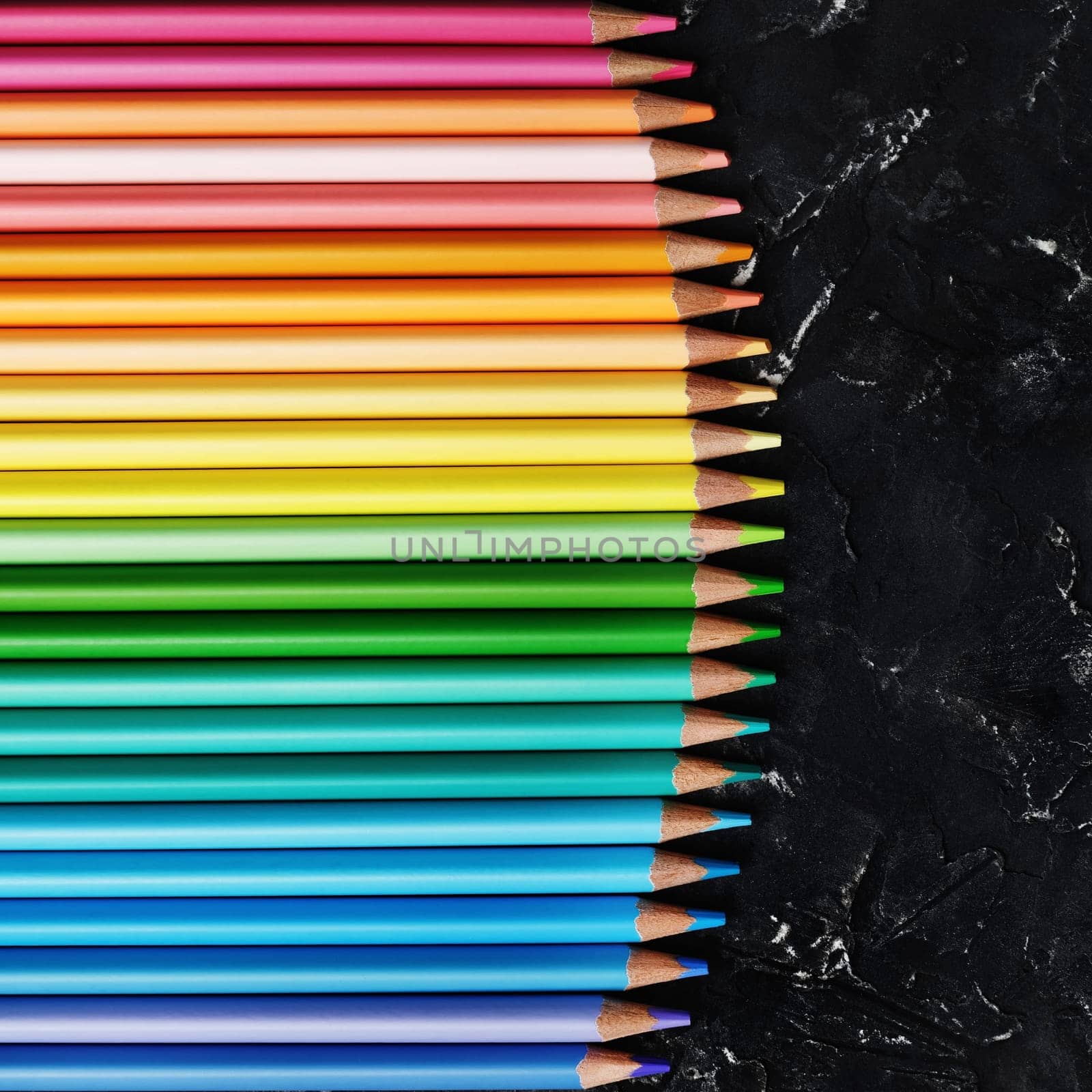 Coloured pencils collection on black plaster background. Row of colourful pencils. Top view.