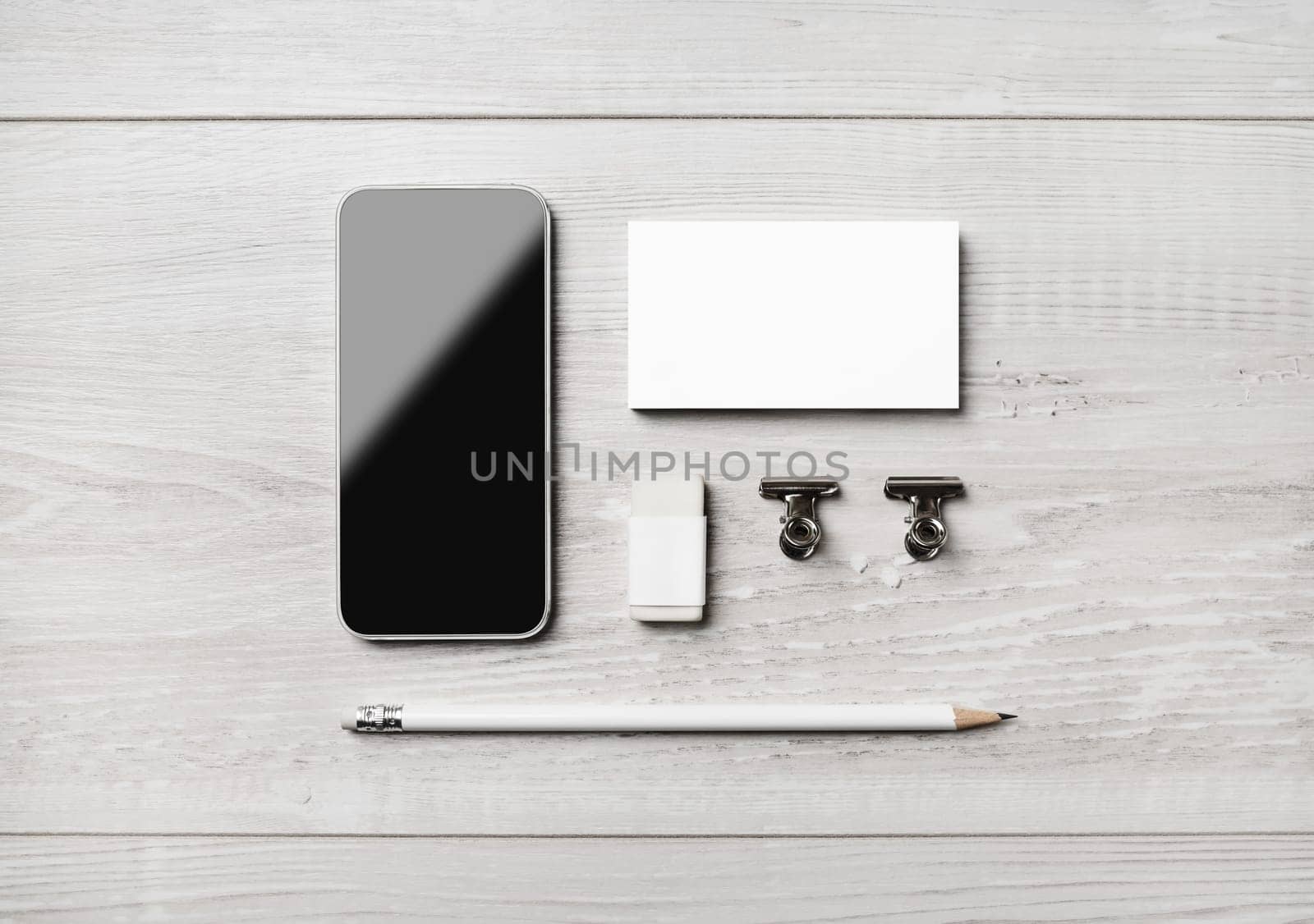 Smartphone and blank stationery: business card, pencil, eraser and clips on light wooden background. Flat lay.