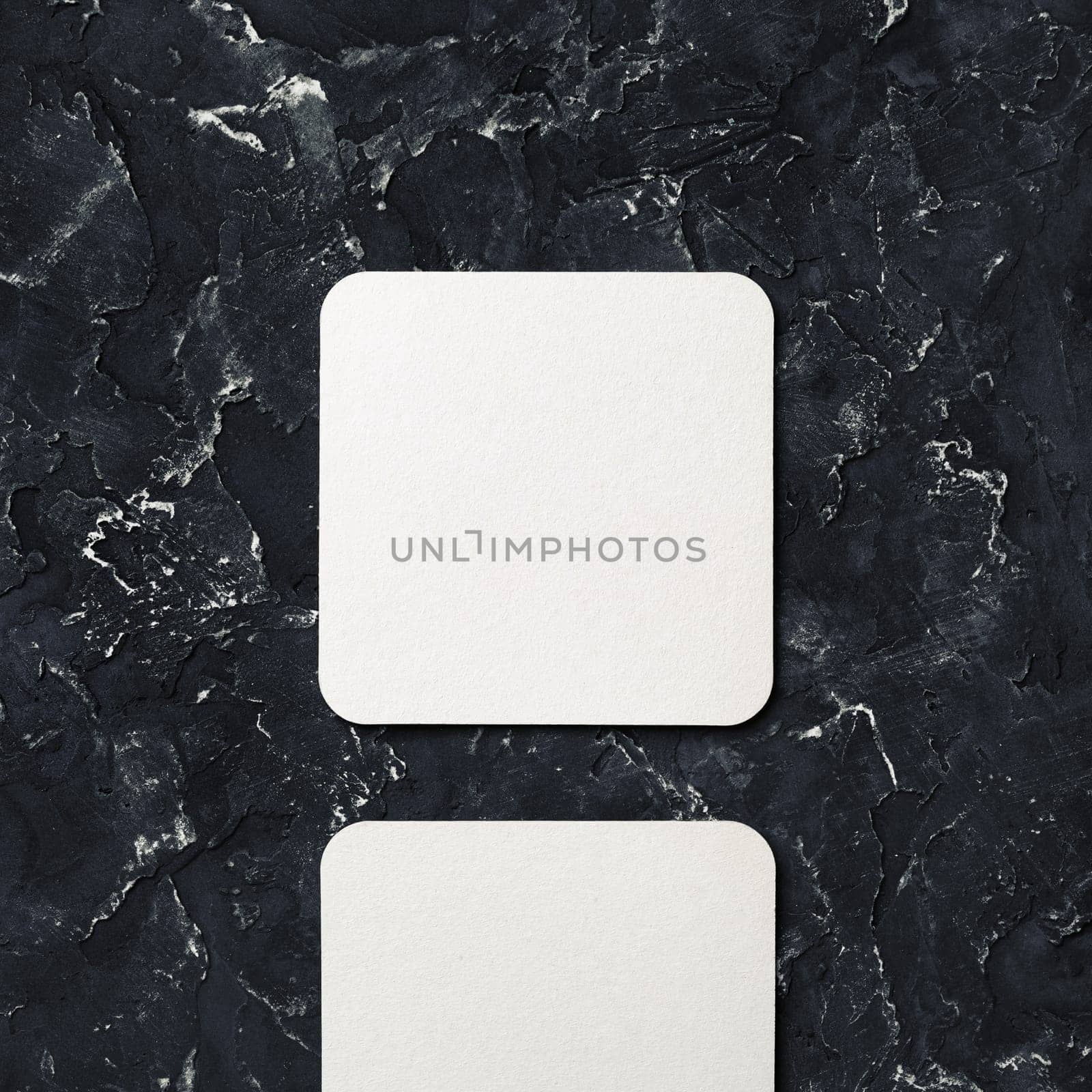 Photo of blank square beer coaster on black plaster background. Blank template for your design. Top view.