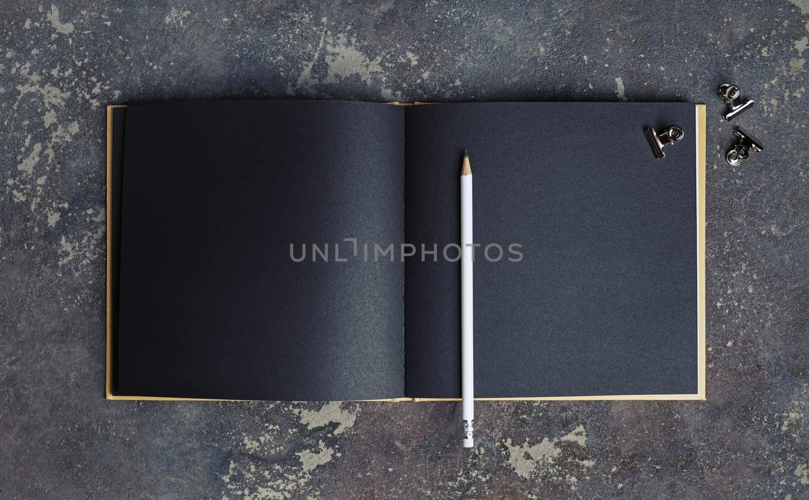 Blank black paper book, pencil and clips on concrete background. Responsive design template. Top view.