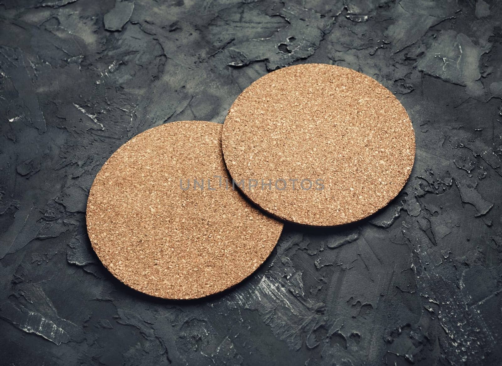 Photo of two blank cork beer coasters on black plaster background. Blank template for your design.