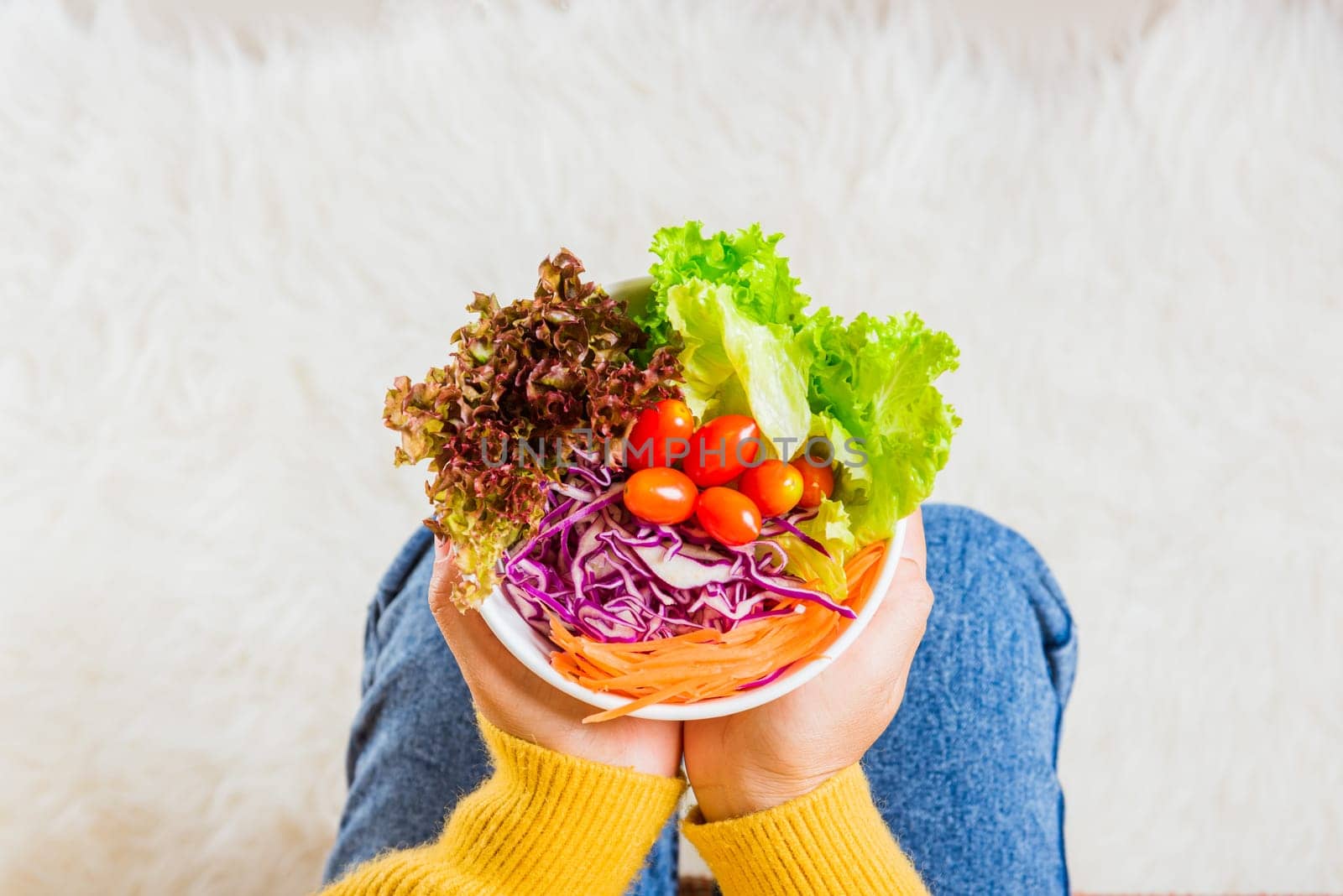 Female hands holding bowl with green lettuce salad on legs, Above young woman eating fresh salad meal vegetarian spinach in a bowl, Clean detox healthy homemade food concept