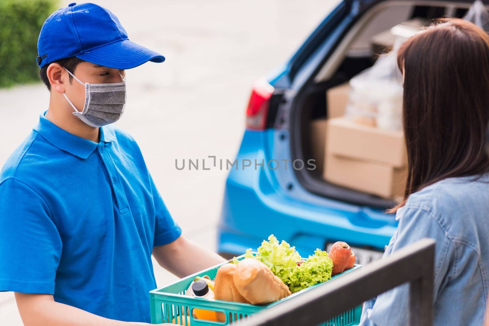 Asian young delivery man wear face mask making grocery fast service giving fresh food vegetable in plastic basket to woman customer receive at house door after pandemic coronavirus, Back to new normal
