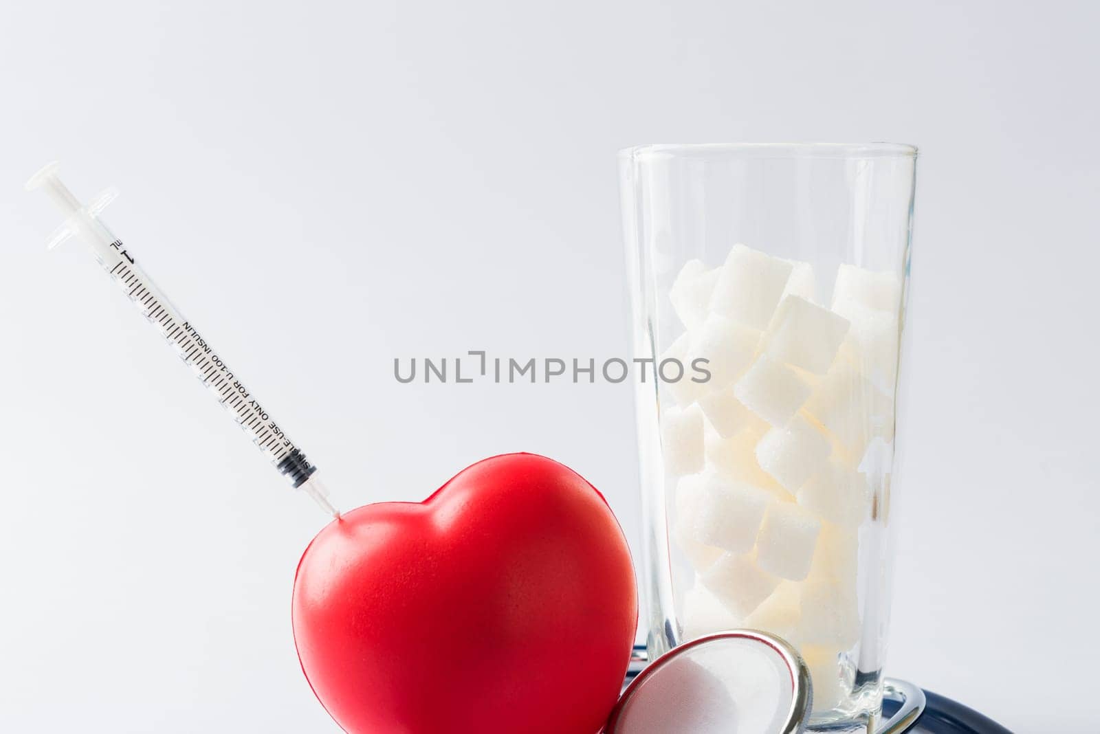A glass full of white sugar cube sweet food ingredient and doctor stethoscope, studio shot isolated on white background, health high blood risk of diabetes and calorie intake concept and unhealthy drink