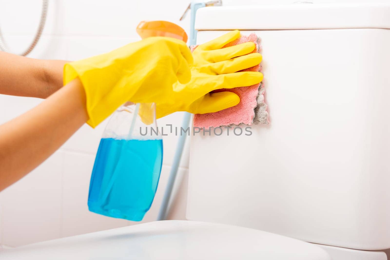 Hand of Asian woman cleaning toilet seat using liquid spray and pink cloth wipe restroom at house, female wearing yellow rubber gloves she sitting cleanup bowl bathroom, Housekeeper healthcare concept
