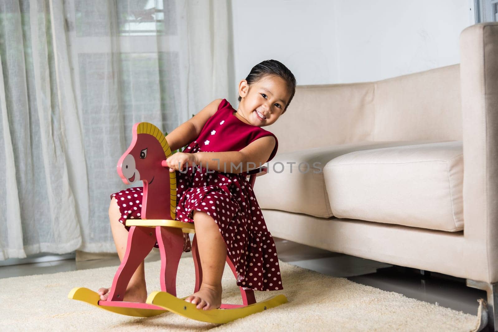 Asian cute little girl swinging riding toy horse, Smiling kid playing horse rocking chair at home in living room, Happy time to play during self kindergarten preschool