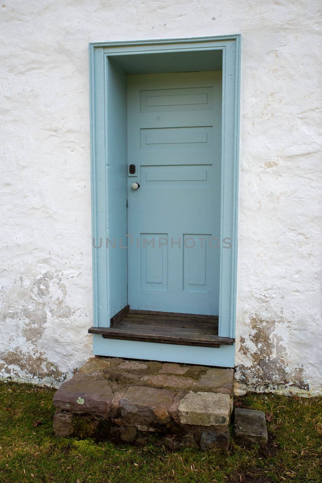 Quaint and charming closed light blue door with stone staps in a whitewashed weathered stone cottage. No people shot outdoors in natural light with copy space.