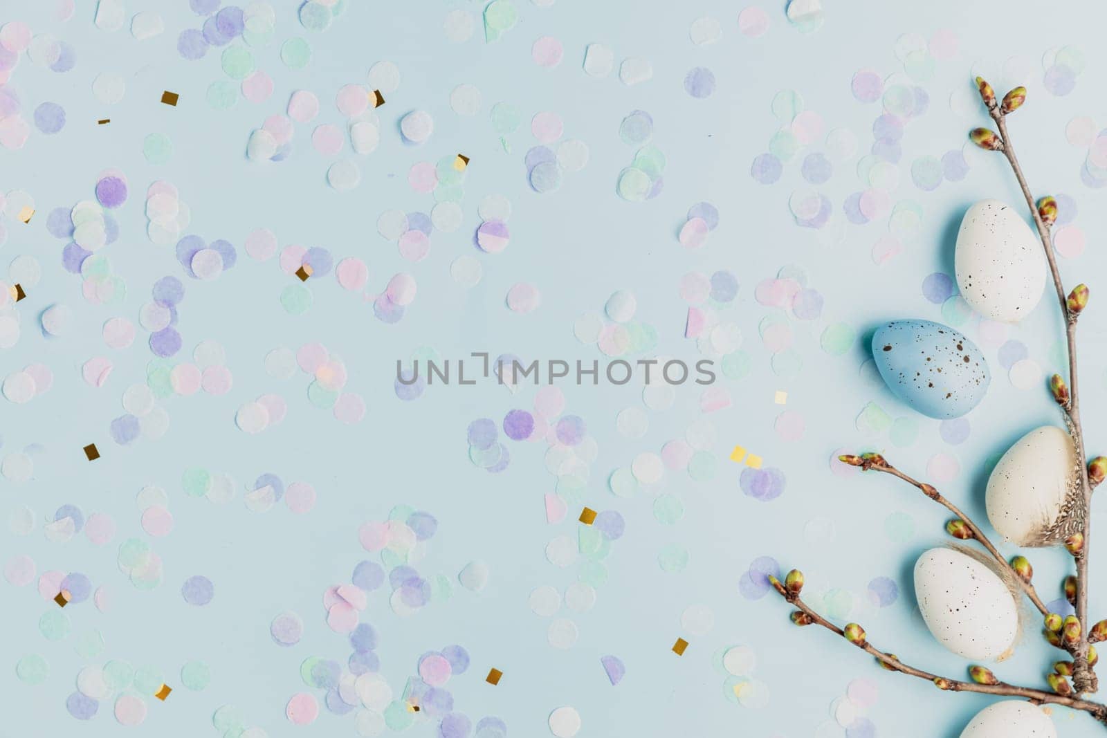 Happy Easter holiday, spring concept. Flat lay with tree branches, flower twigs with white, colorful quail eggs. Blue table background, copy space. Easter home decoration, greeting card, invitation