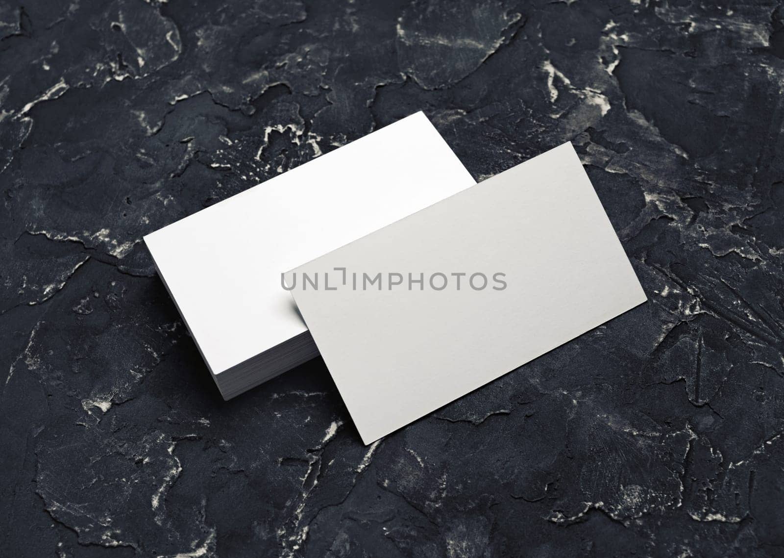 Photo of blank white business cards on black plaster background. Mock-up for branding identity. Blank template for design presentations and portfolios.