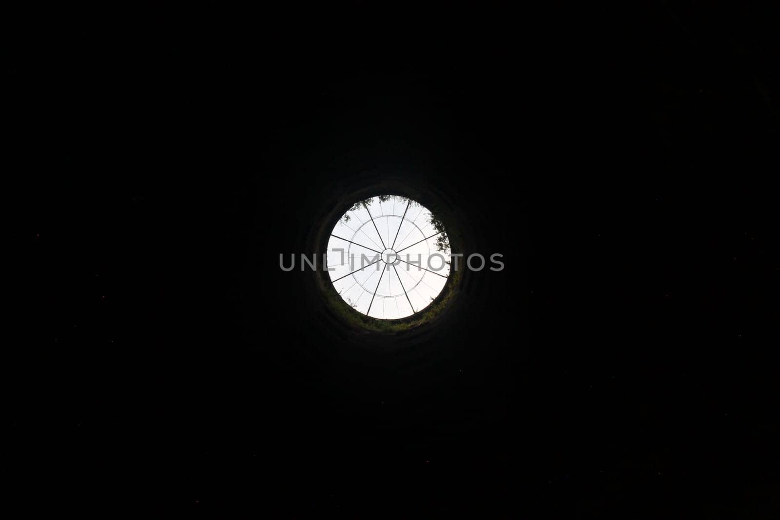 A view of the top of the well from the bottom with the metal grate on the top and the sky with all the black walls around