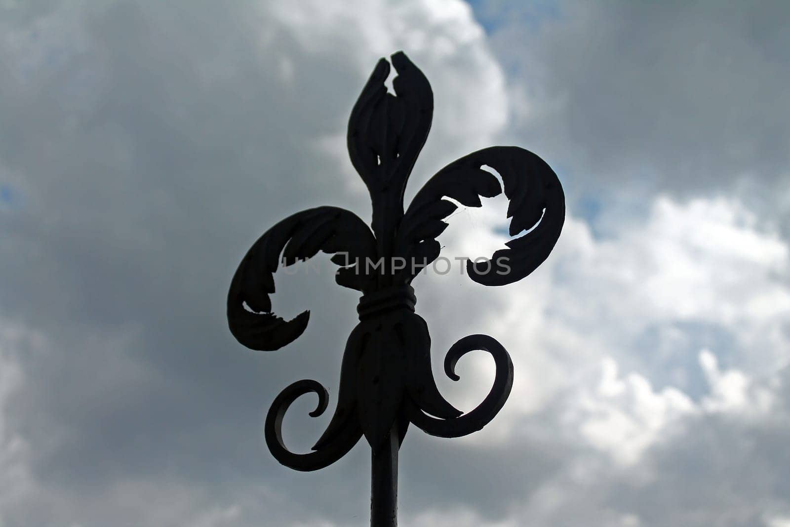 The iron lily on the top of a tower with a dramatic clouded sky in Italy