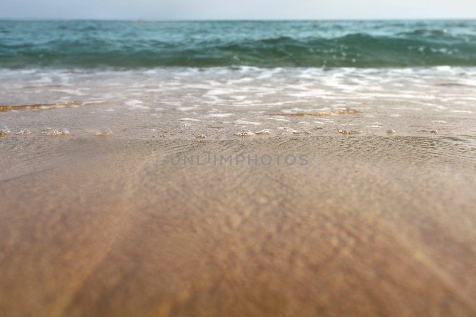 Low angle photo from ground level - beach sand wet from sea, drops of water in air, small waves and blurred ocean in distance. Abstract vacation background.