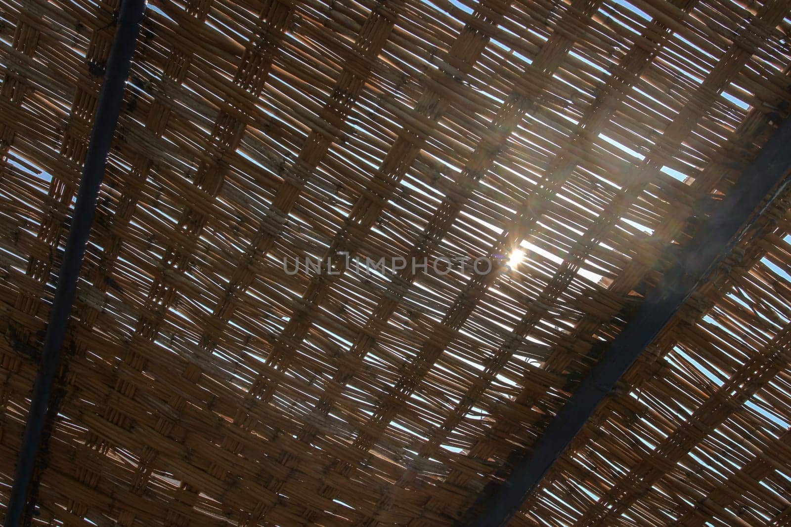 View through palm leaves roof, sun shining behind. Abstract tropical background.