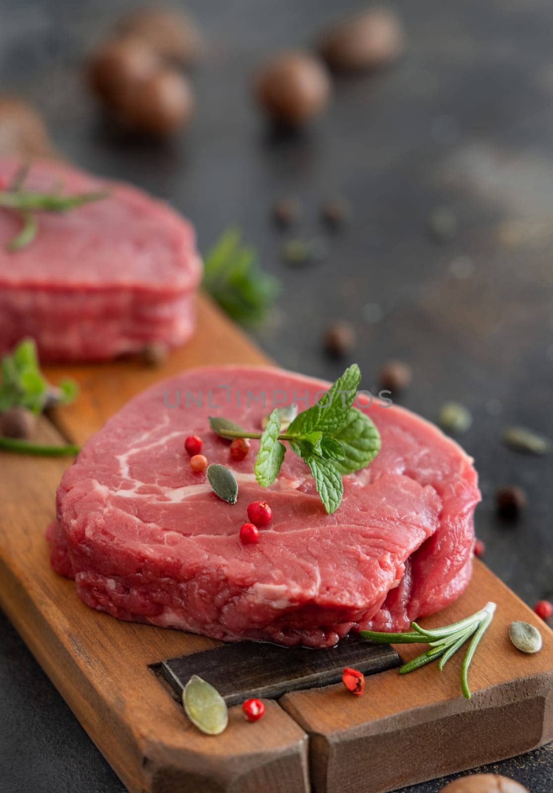 Raw beef fillet steaks on wooden board on dark background close up. Portioned fillet mignons with spices and herbs. Concept of summer food, bbq