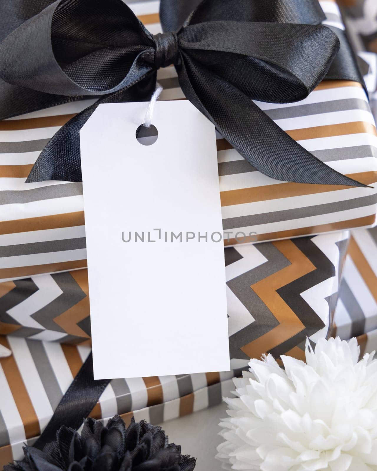 Present with blank vertical gift tag and black bow close up. Gift boxes wrapped in Striped and chevron geometric paper near black and white decor. Christmas, New Year, Birthday, Anniversary label mockup