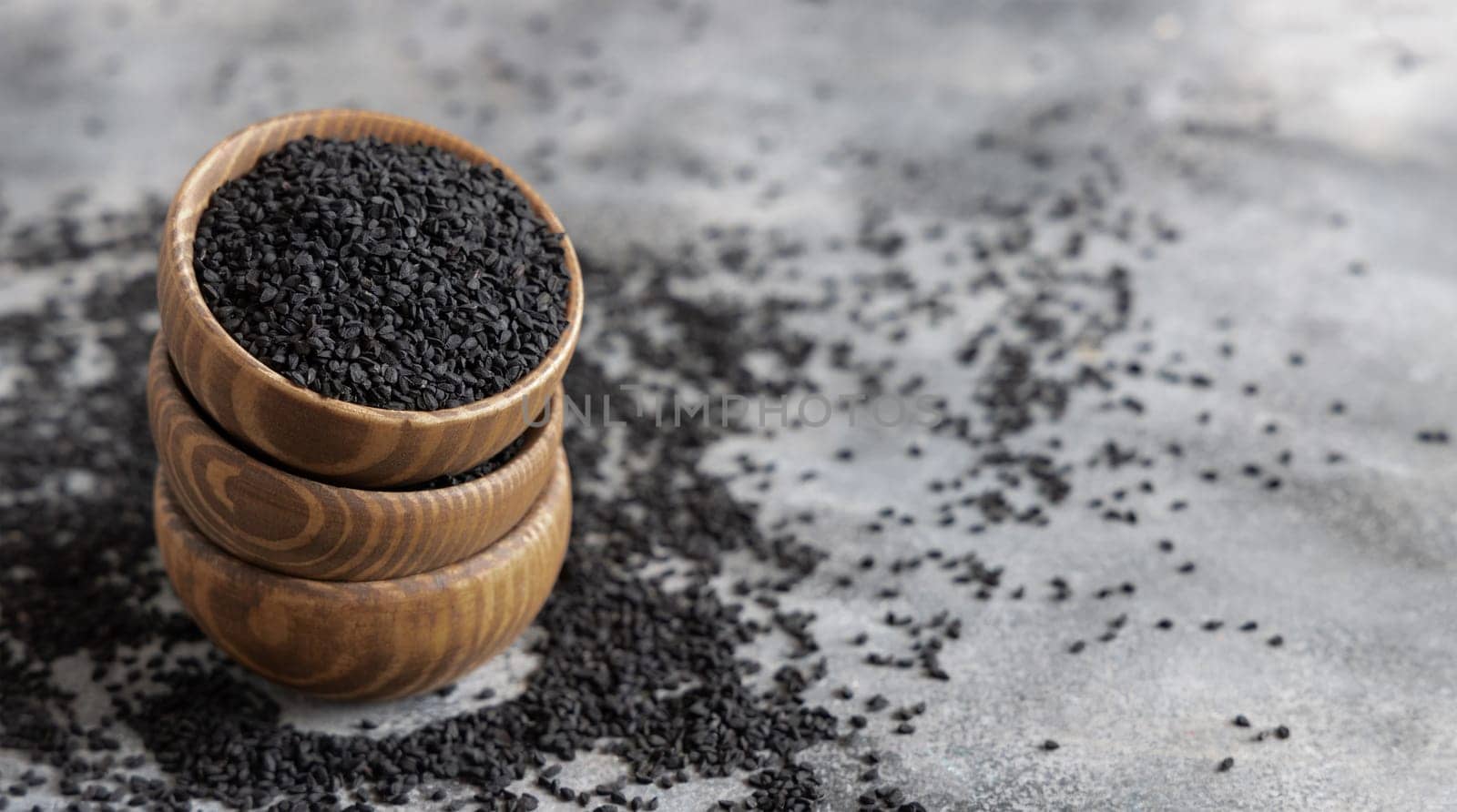 Indian spice Black cumin (nigella sativa or kalonji) seeds in wooden bowls on grey table close up with copy space. Traditional medicine, healthy and vegetarian food concept.