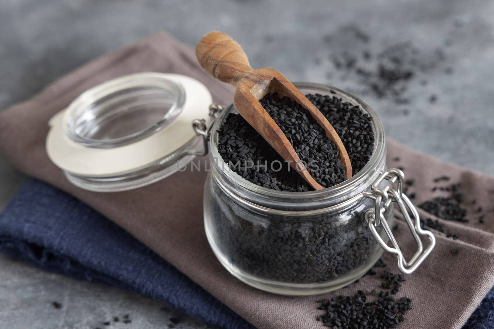 Indian spice Black cumin (nigella sativa or kalonji) seeds glass jar with a wooden scoop, close up. Traditional asian medicine, healthy and vegetarian food concept
