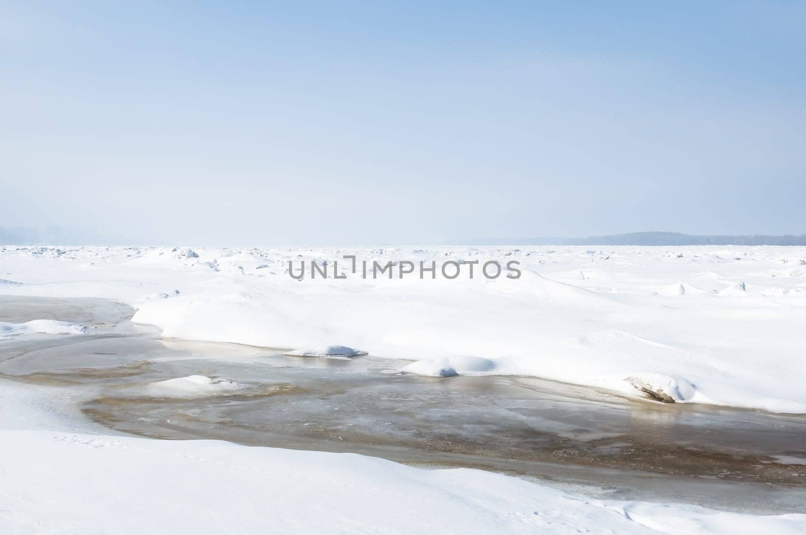 Stunning view of the frozen river covered with chunks of ice and white frosted snow. Snowy desert. The river breaks through the ice.