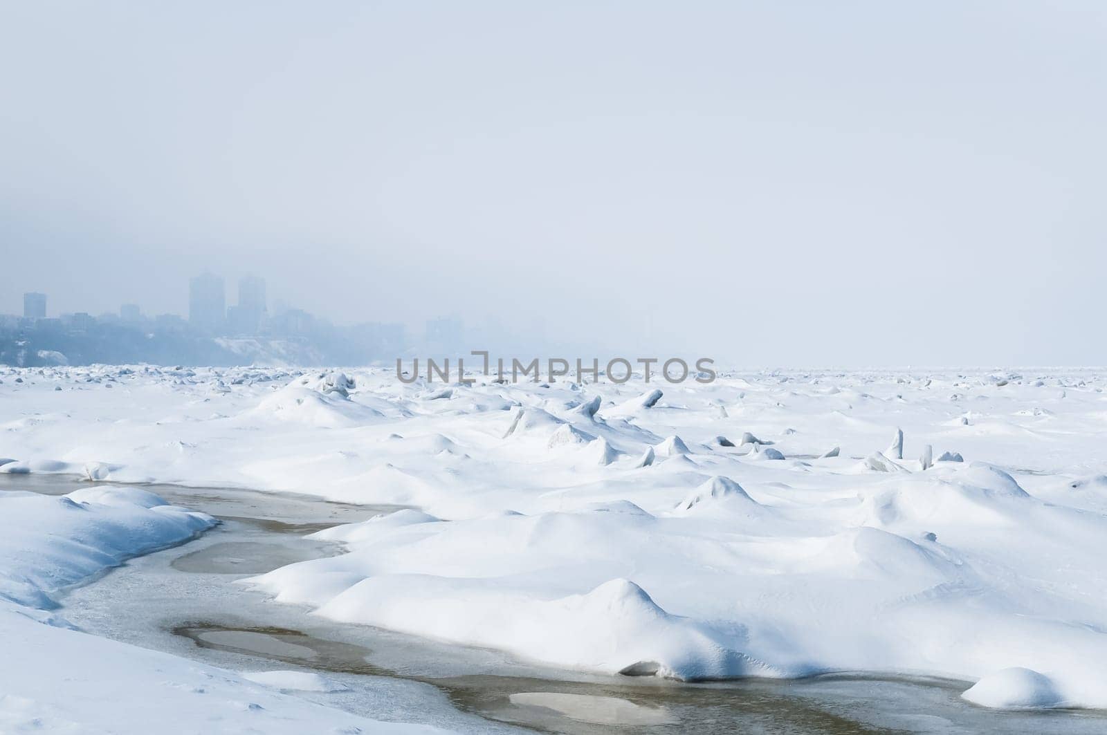 Stunning view of the frozen river covered with chunks of ice and white frosted snow. Snowy desert. The river breaks through the ice.